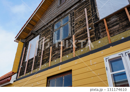 Old wooden house under renovation with new yellow siding and insulation installation process 131174610
