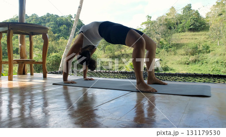 Bridge pose performed on bamboo hut terrace with view of rice paddies and natural greenery Bridge pose performed on bamboo hut terrace with view of rice paddies and natural greenery 131179530