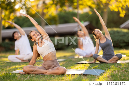 Girl performing stretches in lotus position during group yoga outdoors Girl performing stretches in lotus position during group yoga outdoors 131181172