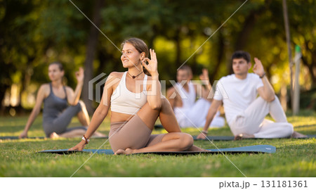 Girl performing twisting asana Matsyendrasana on green meadow Girl performing twisting asana Matsyendrasana on green meadow 131181361
