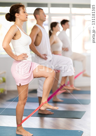 Young woman practicing hip workout with band standing on mat Young woman practicing hip workout with band standing on mat 131181385