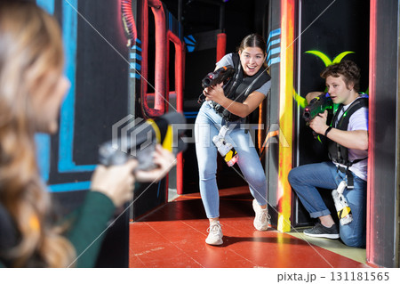 Positive girl holding laser pistol playing laser tag game with friends Positive girl holding laser pistol playing laser tag game with friends 131181565