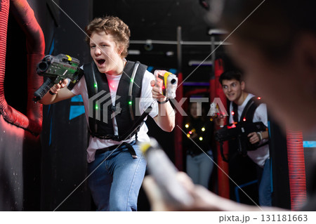 Emotional man with laser pistol playing laser tag with friends on dark labyrinth Emotional man with laser pistol playing laser tag with friends on dark labyrinth 131181663