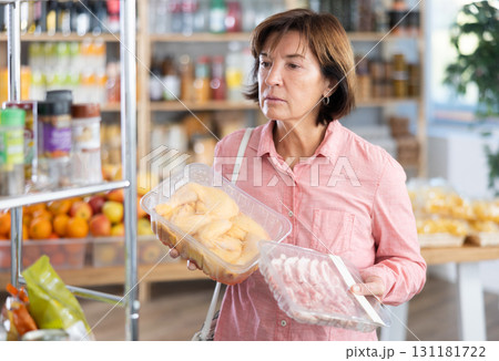 Female buyer carefully reads labels on packaging of semi-finished chicken or pork products - she chooses best product in supermarket 131181722