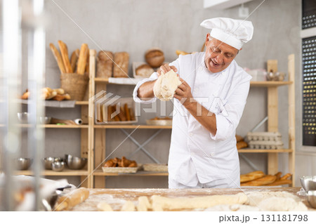Elderly male baker kneading dough on table 131181798