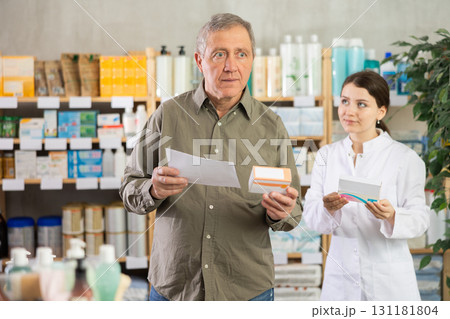 Senior man with doctors prescription selects pills,pharmacist in background 131181804