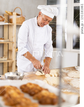 Experienced aged baker portioning dough on floured table 131181861