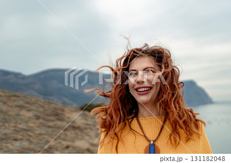 Portrait windswept hair happy woman against a backdrop of mountains and sea. Daylight illuminates the tranquil outdoor setting 131182048