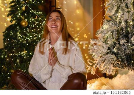 Woman Christmas Tree Prayer Festive Season - A woman sits in front of a Christmas tree, holding her hands in prayer, during the festive season. 131182066
