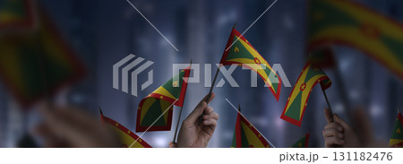 Grenada flags in their hands on a blurred urban background 131182476