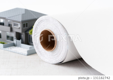 ミニチュアの家と白い壁紙シートのロールのクローズアップ 131182742