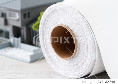 ミニチュアの家と白い壁紙シートのロールのクローズアップ 131182746