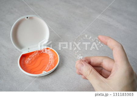 歯科矯正用のアライナーを持つ手とオレンジ色と白色のケース 131183303