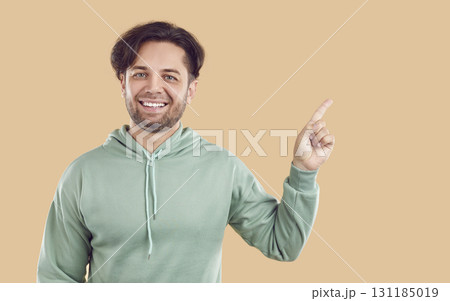 Smiling laughing happy bearded man is pointing index finger on copy space on beige background. 131185019