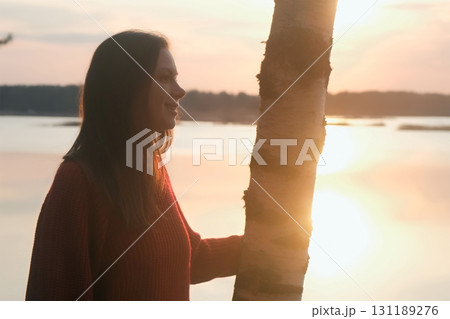 Thoughtful smiling woman admiring nature, lake in dark at sunset in summer. 131189276