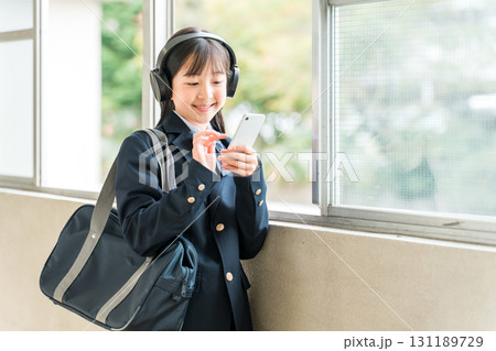 学校の廊下でヘッドフォンで音楽を聴く制服姿の小学生,中学生,高校生の女の子 131189729