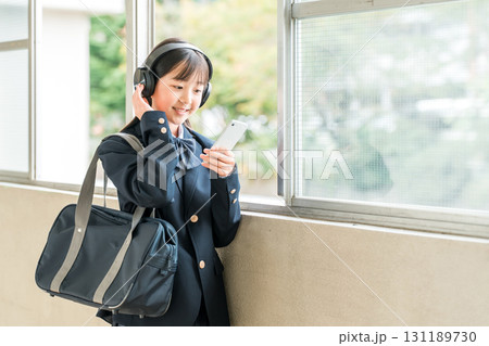 学校の廊下でヘッドフォンで音楽を聴く制服姿の小学生,中学生,高校生の女の子 131189730