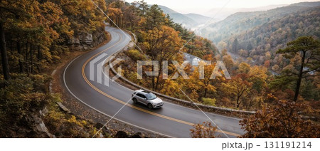 A single white car drives along a winding road through a misty, mountainous forest during the vibrant and colorful autumn season 131191214
