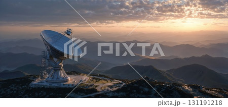 A satellite dish stands on a mountaintop, overlooking a vast, rolling mountain range under a beautiful sunset sky, symbolizing communication and discovery 131191218