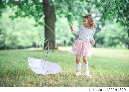 Little girl dancing freely beside her umbrella lying on the grass. A lighthearted and expressive moment of movement and joy in the rain. 131191830