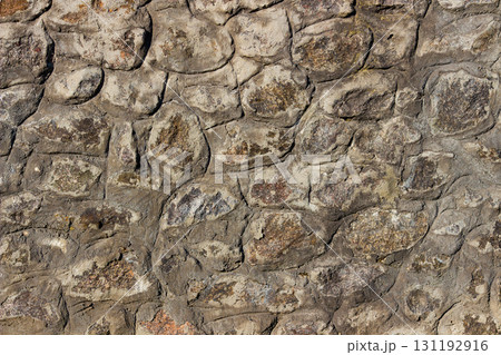 Old stone wall with irregular natural rocks set in mortar. Weathered textures, earthy tones, rough patterns, ideal for background, design element in architectural, historical, rustic-themed designs 131192916