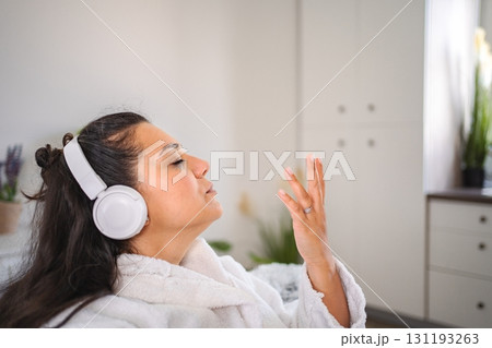 Young woman wearing bathrobe listening to music with headphones at home Young woman wearing bathrobe listening to music with headphones at home 131193263