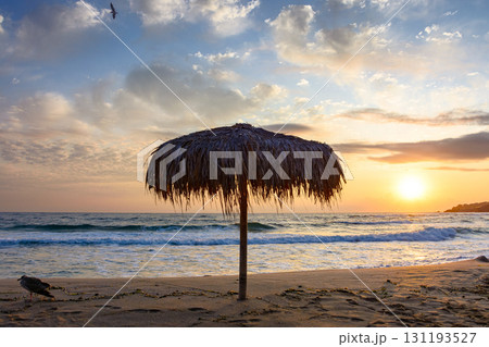 umbrella on the sand beach at sunrise. summer vacation at the sea. blue sky with glowing clouds. beautiful landscape for travel with sun above horizon. tranquil scenery in orange light 131193527