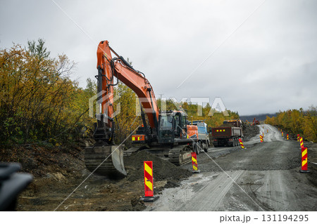 Excavator and trucks working on rural road construction in autumn forest Excavator and trucks working on rural road construction in autumn forest 131194295