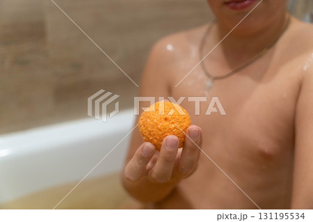 Child holding bright orange bath bomb in bathtub 131195534