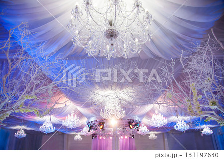 Elegant event hall with chandeliers and decorative trees during a special celebration Elegant event hall with chandeliers and decorative trees during a special celebration 131197630