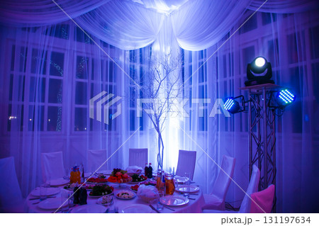 Elegant dining setup with blue lighting and decorations for a special event in a banquet hall Elegant dining setup with blue lighting and decorations for a special event in a banquet hall 131197634