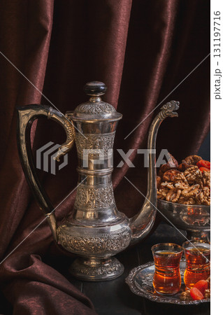 Still life with Ancient East crockery - jug for water or tea, vase with dried fruit and plate with tea in armuda glasses 131197716