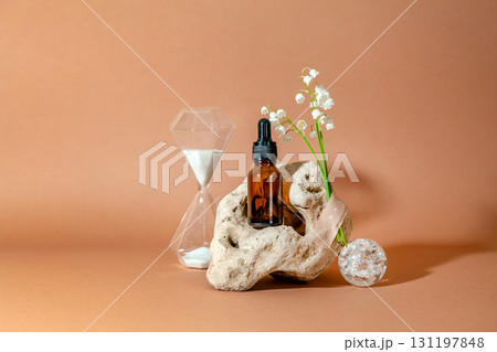 Modern still life with serum bottle on background of unusual natural stone, with bouquet of lilies of the valley and hourglass. The concept of anti-aging care products 131197848