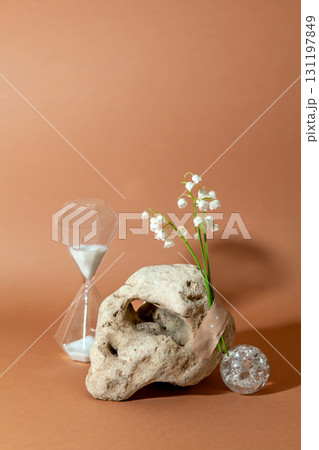 Modern still life with unusual natural stone, with bouquet of lilies of the valley and hourglass. Concept of anti-aging care products. Empty podium for cosmetics organic products and others 131197849