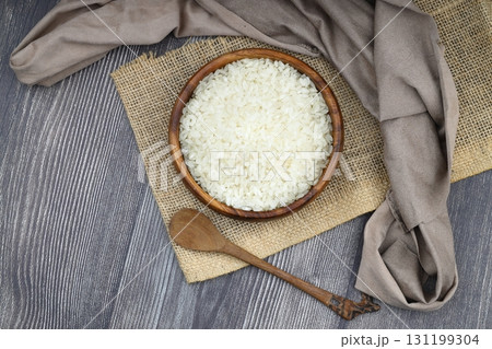 Raw white rice on wooden background. Long uncooked rice in wooden plate. Natural organic food. Traditional Asian cereal culture. 131199304
