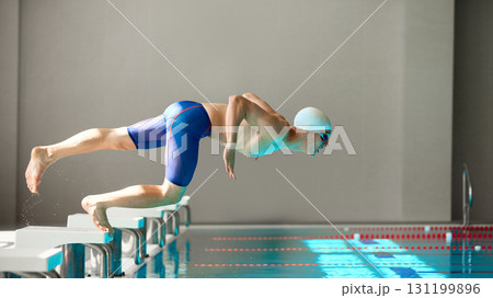 Swimmer in streamlined dive motion launching into pool from starting block 131199896