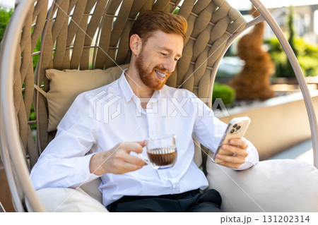 Ginger bearded professional enjoying hot drink outdoors using phone online 131202314