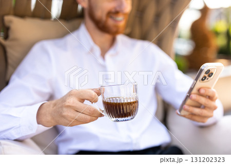 Bearded man in white shirt relaxing with cup of coffee and smartphone browsing internet 131202323