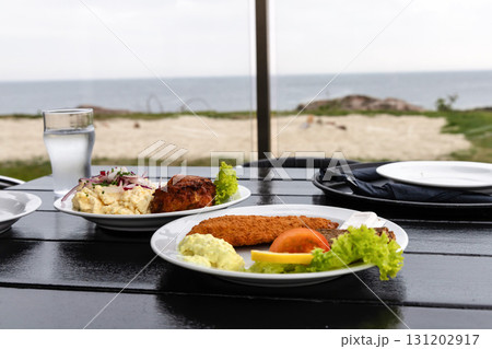 Seafood restaurant on the seashore. White plate with fish patties, fish fillets and potato salad. Seafood restaurant on the seashore. White plate with fish patties, fish fillets and potato salad. 131202917