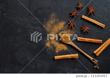 Aromatic cinnamon sticks, cinnamon powder and anise on black table, flat lay. Space for text 131203457