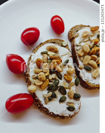 Whole grain toast with cream cheese, seeds, peanuts and cherry tomatoes. Whole grain toast with cream cheese, peanuts and mixed seeds, served with fresh cherry tomatoes on a white plate. Homemade vege 131203473