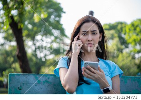 A woman appears thoughtful while using her smartphone in a park on a sunny day. A woman appears thoughtful while using her smartphone in a park on a sunny day. 131204773
