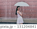 A young woman stands gracefully under an umbrella, smiling amidst a serene backdrop of flowing water. 131204841
