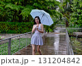 A young woman strolls on a rainy day, holding a light umbrella, embracing the refreshing atmosphere of nature. 131204842