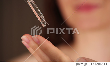 Young woman holding a dropper with serum for face. Facial oil fall from a glass pipette, macro view. Selective focus. Cosmetic background with liquid skincare product. Beauty treatment concept. Young woman holding a dropper with serum for face. Facial oil fall from a glass pipette, macro view. Selective focus. Cosmetic background with liquid skincare product. Beauty treatment concept. 131206511