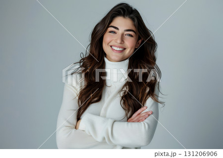 A joyful young woman stands with her arms crossed, exuding confidence and warmth in a simple, light-colored backdrop 131206906
