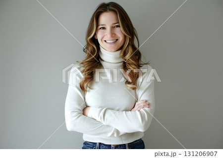 Woman with long hair smiles confidently while wearing a white turtleneck sweater, arms crossed, in a bright indoor setting 131206907