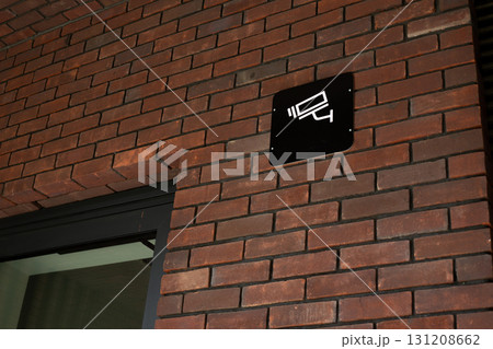 Security camera sign mounted on brick wall, indicating surveillance, commonly seen in commercial and residential properties to enhance safety and monitor activity Security camera sign mounted on brick wall, indicating surveillance, commonly seen in commercial and residential properties to enhance safety and monitor activity 131208662