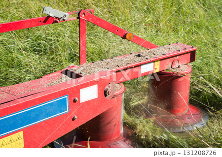 Red mechanical grass mower in action in a field  131208726