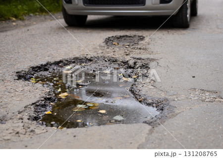 Concept of roads and highways in terrible condition. Modern silver car stopped near huge pothole in the middle of the road in order not to damage vehicle Concept of roads and highways in terrible condition. Modern silver car stopped near huge pothole in the middle of the road in order not to damage vehicle 131208765
